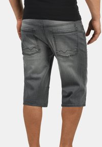 Shorts de mezclilla gris con un ajuste relajado, hasta la rodilla, que presentan dos bolsillos traseros con detalles de costura y tonos desvanecidos.