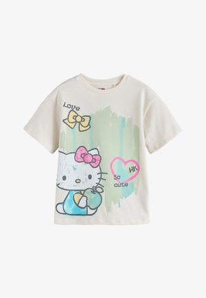 Nuori tyttö, jolla on laineikkaat ruskeat hiukset, pukeutuneena valkoiseen Hello Kitty -t-paitaan, jossa on rusetteja, sydän jossa teksti "so cute" ja vaaleansinisiä sekä vihreitä maaliläiskiä.