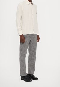 Light-colored, long-sleeve shirt with vertical stripes, paired with gray textured trousers and black leather shoes.