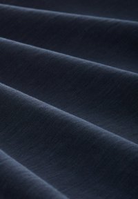 Tejido de un azul marino oscuro con una textura suave, que presenta un brillo sutil y está doblado en ondas, mostrando un patrón suave y consistente en toda la superficie.