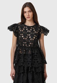 Black peplum top made of embroidered fabric featuring intricate cut-out patterns and puff sleeves. Textured lace accents throughout.