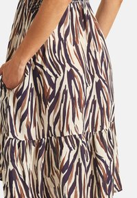 Geprinte jurk met een lichtgekleurde stof met bruine en donkerblauwe zebrapatronen, elastische taille, en gelaagde ruches aan de onderkant, met zijzakken.