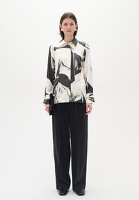 Black and white patterned silk button-up shirt with a collar, paired with high-waisted black trousers and sleek black shoes.