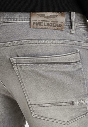 Nahaufnahme der Tasche einer grauen Jeans aus Denim mit gesticktem "PME"-Logo und einem Lederpatch darüber mit der Aufschrift "Air Transport Service PME Legend."