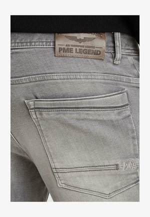 Nahaufnahme der Tasche einer grauen Jeans aus Denim mit gesticktem "PME"-Logo und einem Lederpatch darüber mit der Aufschrift "Air Transport Service PME Legend."
