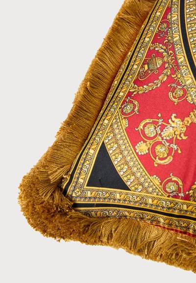 Piros és fekete mintás párna arany szegélyekkel és rojttal. Bonyolult mintákat ábrázol díszes motívumokkal és texturált felülettel.