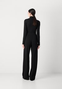 Maglietta nera a maniche lunghe con collo alto e pantaloni a gamba larga, realizzati in tessuto morbido. Design minimalista con vita aderente e silhouette fluida.