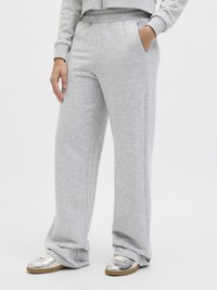 Light gray sweatpants made of soft, textured fabric with a loose fit, elastic waistband, and side pockets. Paired with silver sneakers.