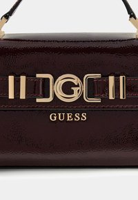 Borsa a mano in pelle verniciata color marrone scuro con accessori in finitura oro, caratterizzata da una chiusura con logo e cuciture decorative. Forma rettangolare compatta.