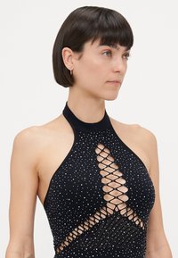 Black halter top with shimmering embellishments and a crisscross cutout design. Smooth texture, form-fitting shape, and minimalistic neckline.