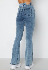 Ljusblå utsvängda jeans i denim, med bakfickor och hög midje-design. Tyget har en subtil textur och klassisk sömnad.