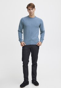 Light blue wool sweater with a crew neckline, paired with dark gray jeans and black shoes. Smooth texture, fitted design, and long sleeves.