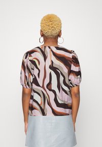 Blusa de manga curta com um padrão abstrato multicolorido, apresentando tons de rosa, castanho e creme. A parte de trás tem um detalhe em forma de lágrima e mangas bufantes.