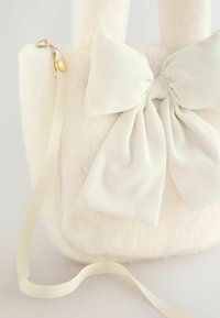 Geantă de mână din blană albă, cu o fundă mare și moale din material textil pe față. Are o curea din panglică și o închizătoare cu capse aurie.
