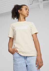 Svijetlosmeđi pamučni majica s velikim bijelim Puma logotipom na prednjoj strani. Kratki rukavi i klasičan kroj oko vrata.