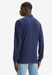 Marineblauwe polo met lange mouwen en een klassieke kraag, met een gladde textuur en een aangesloten ontwerp, gecombineerd met lichtblauwe jeans.