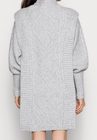 Ljust grått stickat klänning med hög krage, med texturerade kabelmönster och ribbade detaljer på ärmar och fåll.
