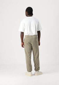 Olivenfargede joggebukser med avsmalnende ben og elastisk midje, kombinert med en enkel hvit t-skjorte. Fottøyet er lyse sneakers.