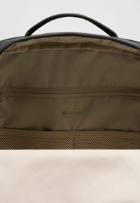 Zwarte backpack interieur met tan voering, een ritsvak en een gaassectie. Bevat minimale branding en een gladde stoftextuur.