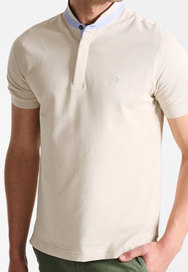 Light beige polo shirt with a blue collar, worn by a man with a neutral expression. The background is light and untextured.