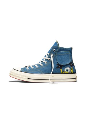 Basket haute en denim bleu avec lacets blancs, semelle en caoutchouc, poche latérale et personnage de dessin animé qui émerge de la zone du talon.