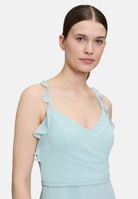 Jasnoniebieska sukienka z falbaniastymi ramiączkami, głębokim dekoltem w kształcie litery V oraz dopasowanym fasonem z gładkiej tkaniny, tworząca elegancką sylwetkę.