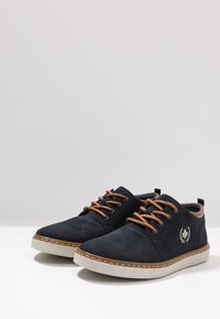 Scarpe in suede nere con lacci color nocciola, punta tonda e suola in gomma bianca. Presentano un logo ricamato e cuciture decorative lungo la suola.