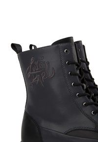 Botas de tobillo de cuero negro con punta redonda, diseño bordado de "Love", ojales de metal y cierre de cordones. Lengüeta en la parte posterior para facilitar el uso.