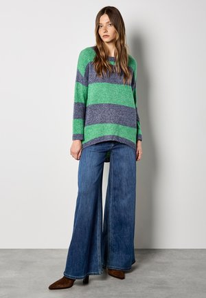 Gestreifter Pullover in Grün und Marineblau, gestrickte Textur, übergroßer Schnitt. Kombiniert mit weit geschnittenen Jeans und spitzen braunen Stiefeletten.