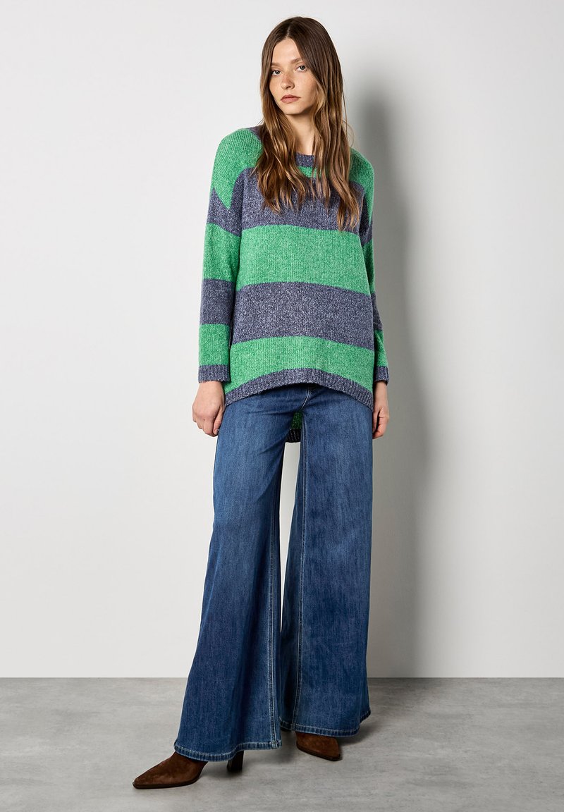 Gestreifter Pullover in Grün und Marineblau, gestrickte Textur, übergroßer Schnitt. Kombiniert mit weit geschnittenen Jeans und spitzen braunen Stiefeletten.