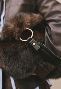 Geantă maro din blană artificială cu un inel circular din metal auriu, prevăzută cu o curea neagră din piele cu cusături și un detaliu cu nasture de tip capse.