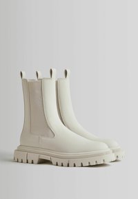 White ankle boots with a smooth rubber finish, side mesh panels, and chunky textured soles. Features pull tabs on the tops for easy wear.