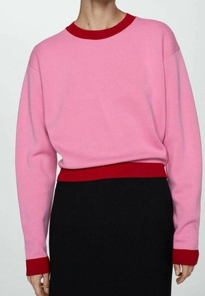 Personne portant un pull rose à manches longues avec col, poignets et ceinture rouges, associé à une jupe noire.