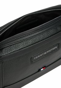 Schwarze Leder-Clutch mit strukturierter Oberfläche, ausgestattet mit einem Reißverschluss, einem Innenfach und einem Etikett, das "TOMMY HILFIGER" liest.