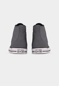 Ζευγάρι γκρι ψηλά sneakers Converse All Star, εμφανιζόμενα από πίσω, με λευκές σόλες και μαύρα λογότυπα στα τακούνια.