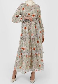 Blomster maxi kjole i lysegrøn gennemsigtig stof med lagdelte lag. Har orange og lyserøde blomster, lange ærmer og et bælte i taljen.