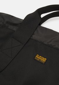Sac cabas en tissu noir avec coutures renforcées aux poignées et petit patch logo G-Star Originals Raw Denim jaune et noir.