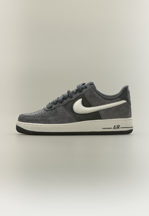 Baskets basses Nike Air grises avec un Swoosh blanc et une semelle blanche, vues de profil sur un fond uni.