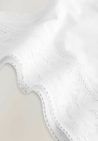 Vêtement blanc avec un délicat bord en dentelle présentant un motif floral et des bords festonnés, fabriqué à partir d'un tissu doux et lisse.