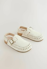 Chaussures blanches en daim à enfiler avec des détails tressés, boucle métallique ajustable, semelle intermédiaire en liège et doublure intérieure lisse.
