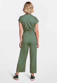 Mono verde con estampado, de manga corta, con cintura ajustada, diseño de pierna ancha y acentos geométricos en amarillo y naranja. Calzado casual.
