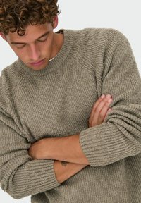 Suéter gris de punto acanalado con cuello redondo. El suéter presenta un tejido texturizado y un corte relajado, con puños doblados y sin marcas visibles.