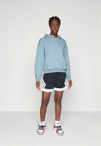 Hellblauer Kapuzenpullover mit vorderer Tasche und Kordelzug, kombiniert mit schwarzen Shorts mit weißen Akzenten und Design. Getragen mit sportlichen Schuhen.