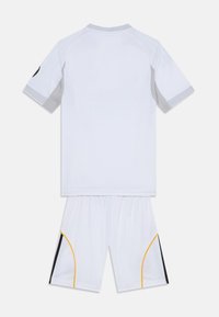 Équipement de sport blanc comprenant un t-shirt à manches courtes et un short. Le t-shirt a un col gris, les shorts présentent des accents latéraux noirs et jaunes. Tissu lisse.