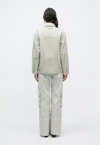 Hellgraue Wildlederjacke mit einfachem Kragen und Rückennaht-Details, kombiniert mit hoch taillierten, weit geschnittenen Cargo-Hosen im gleichen hellgrauen Farbton.
