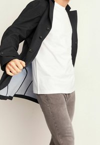 Svart skräddarsydd kappa med knäppning och blått foder, kombinerad med en vit t-shirt och gråa slim-fit byxor. Slät tygkvalitet, strukturerad design.