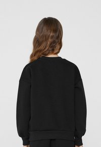 Czarny sweter z okrągłym dekoltem wykonany z miękkiego materiału. Posiada opadające ramiona, ściągacze na rękawach i dole oraz luźny krój. Gładki design bez wzorów.