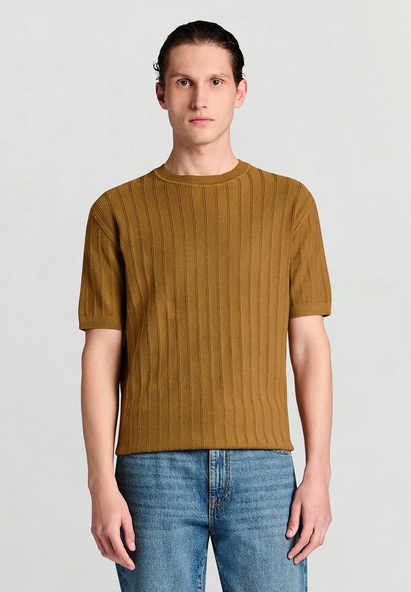 Braunes, geripptes Strick-T-Shirt mit kurzen Ärmeln und Rundhalsausschnitt, kombiniert mit hellblauen Jeans. Der Stoff hat eine strukturierte Haptik und ein gleichmäßiges Muster.