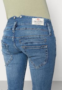 Modré džíny mají střední výšku pasu, zadní kapsy s úhlovými klapkami a vyšitý štítek na pase.