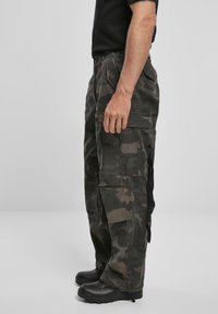 Pantalones cargo en verde oscuro y con patrón de camuflaje negro, que cuentan con múltiples bolsillos, un corte relajado y una textura de tela duradera.